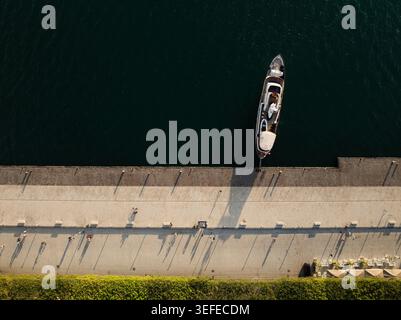 Aerial view of a luxury yacht docked at the Island of Ortigia promenade with people walking and casting long shadows in Syracuse, Sicily, Italy. Stock Photo