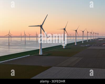 Aerial view of a large wind farm with turbines standing along a coastal dike and in the water at sunset over agricultural fields in Noordoostpolder in Stock Photo