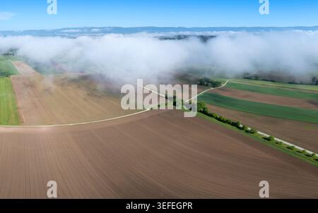Aerial view of agricultural fields with low clouds rolling over the landscape and a winding road in Grossaffoltern, Canton of Bern, Switzerland. Stock Photo