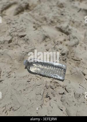 A discarded empty clear plastic water bottle lying on the sand, highlighting environmental pollution on a beach. Stock Photo