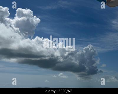A wide shot of a deep blue sky filled with dramatic, thick white cumulus clouds over the ocean horizon. Stock Photo