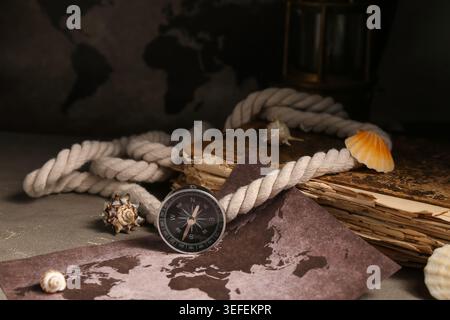 Composition with modern compass, world map, old book, rope and seashells on grey grunge background Stock Photo