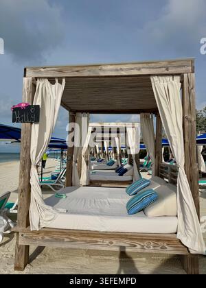 A perspective view of luxury wooden beach cabanas with white curtains and comfortable beds lined up on a resort coast in Nassau, Bahamas. Stock Photo