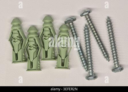 Green plastic drywall anchors and screws flat lay on white background. Stock Photo