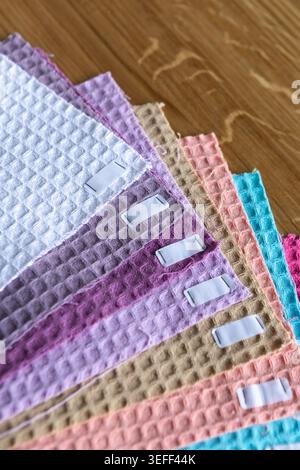 Different fabric samples are displayed on a wooden surface. The samples feature various colors and textures. Some samples have labels attached, showin Stock Photo