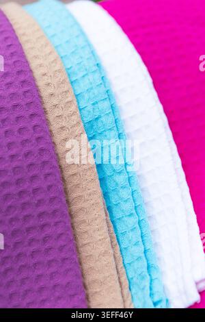 Towels in various colors are arranged in a row on display for customers. The fabrics show different textures and hues in a retail setting. Stock Photo