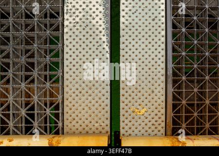 Two metal panels with different patterns are placed next to each other. The wall shows signs of rust and wear with green accents. The area looks negle Stock Photo