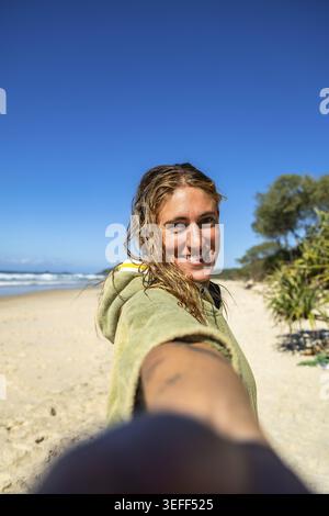 Woman smiling with wet hair after surfing on the gold coast, wearing a cozy poncho on a sunny beach day, enjoying ocean waves, sand, and relaxed summe Stock Photo