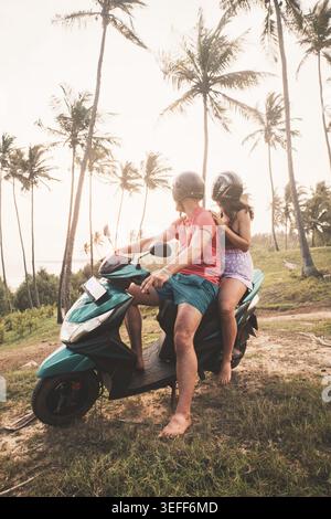Happy smiling couple travelers riding motorbike scooter in safety helmets during tropical vacation under palm trees Sri lanka turtle beach. South coas Stock Photo