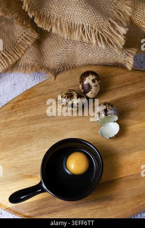 Rustic scene showing small quail eggs and a raw yolk in a black pan, ready for healthy cooking and food preparation Stock Photo