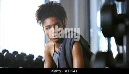 Bodybuilder, tired and woman in gym, thinking or rest with intense training recovery for fitness. Break, sweating and exhausted African person in Stock Photo
