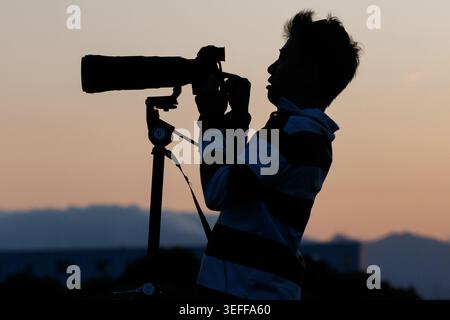 A Japanese man, in silhouette, uses a camera on a tripod to photograph military aircraft on Atsugi airbase, Kanagawa, Japan. Stock Photo