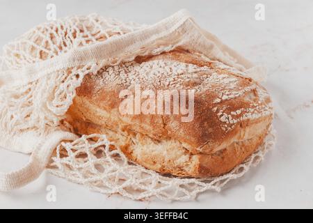 Freshly baked rye bread, ciabatta, in a mesh bag, on a marble light table, natural light Stock Photo