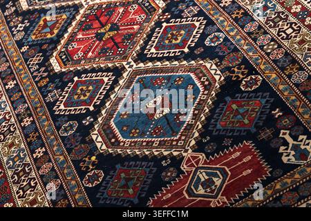Handmade Persian style rug featuring bold geometric medallions and intricate borders in rich red, blue and cream tones, perfect for traditional interi Stock Photo