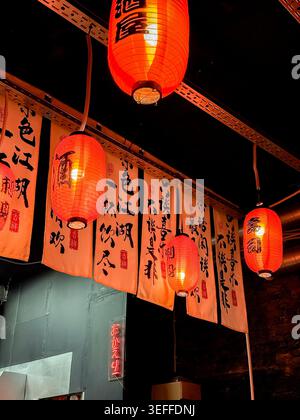 Traditional Japanese red lanterns and decorative calligraphy banners inside a Japanese restaurant with warm ambient lighting Stock Photo