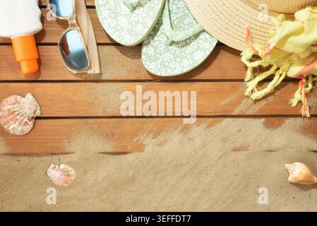 Beach items including flip flops, sunglasses, towel, hat, sunscreen, and shells on a sandy wooden surface with copy space. Stock Photo