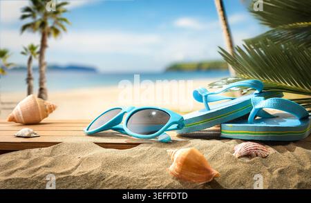 Turquoise flip flops and sunglasses resting on sandy tropical beach with seashells, palm leaves, and blurred ocean background in bright summer sunligh Stock Photo