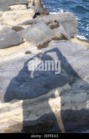 Shadow of couple making heart hand gesture on coastal rock, Miura Kanagawa Stock Photo