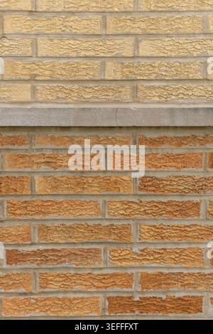 The wall displays two distinct sections of bricks in various shades of yellow and brown. The upper section has a smooth surface, while the lower part Stock Photo