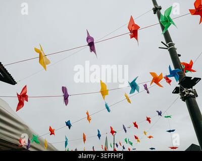 Bright multicolored pinwheels suspended across an outdoor street under a cloudy sky. Playful urban decoration scene ideal for festival, celebration, c Stock Photo
