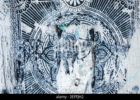 Monochrome geometric mandala pattern painted on a weathered, peeling concrete wall. Textured urban background with cracks and scratches. Stock Photo
