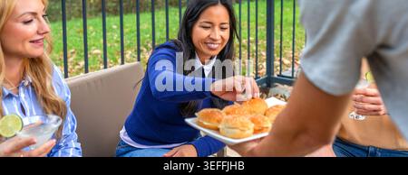 Group of diverse friends relaxing and socializing with drinks and snacks on patio, sharing good moments and lighthearted conversation in outdoor party Stock Photo