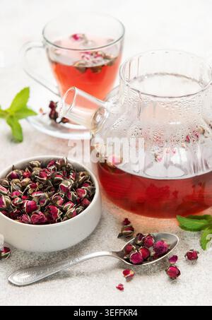 Rose tea brewing in a glass teapot and cup with dried buds and fresh mint Stock Photo