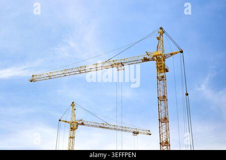 Two massive yellow tower cranes stand tall against a bright, slightly cloudy blue sky, showcasing the impressive scale and engineering of a modern urb Stock Photo