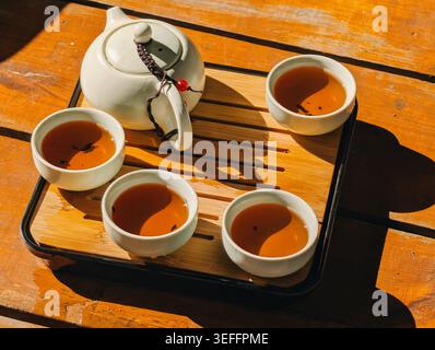 Chinese tea set with white teapot and four cups on bamboo tray. A white ceramic teapot and four cups filled with amber tea on bamboo tray. Stock Photo