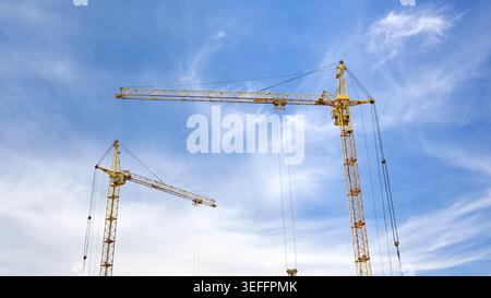Two massive yellow tower cranes stand tall against a bright, slightly cloudy blue sky, showcasing the impressive scale and engineering of a modern urb Stock Photo