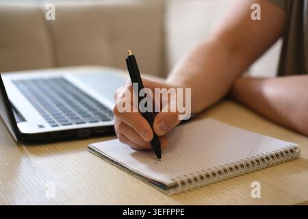 Freelancer writing notes in a notebook beside laptop Stock Photo