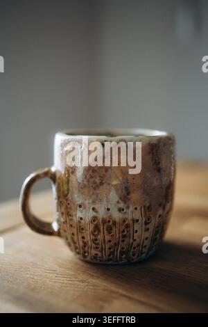 Large rustic handmade ceramic mug with a handle, featuring a distressed brown texture with blue, green, and beige reactive glaze effects. Handcrafted Stock Photo