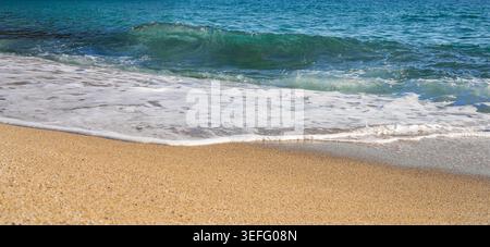 Blue sea wave with white foam rolling onto sandy beach coastline Stock Photo