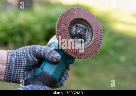 Professional handyman in protective gloves holds a powerful angle grinder with an abrasive flap disc. A concept of confidence, high productivity, and Stock Photo