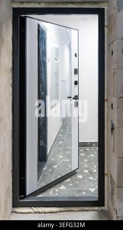 A newly installed metal entrance door featuring a large built-in mirror covered in protective film. Visible mounting foam around the frame highlights Stock Photo