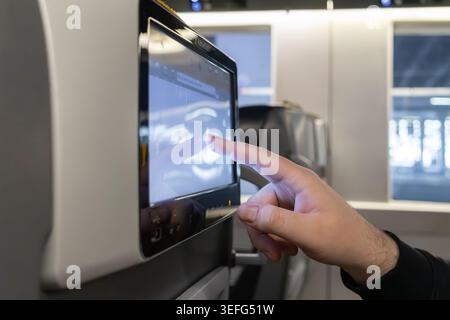A close up of a human finger selecting content on a digital tablet screen mounted on a train seat highlights user interface interaction, wireless conn Stock Photo