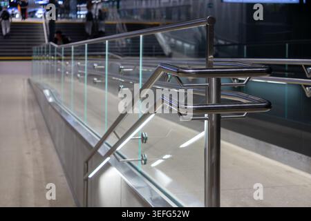 Close up of a sleek metal handrail with integrated LED lighting and transparent glass barriers in a transit hub, emphasizing urban infrastructure, acc Stock Photo