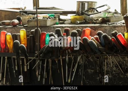 Close-up of various screwdrivers and hand tools stored on a workbench in an industrial workshop, showing organized chaos, craftsmanship and real worki Stock Photo