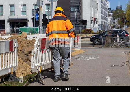 The rear view of a builder in reflective orange workwear inspects city road maintenance, focusing on safety regulations and infrastructure improvement Stock Photo