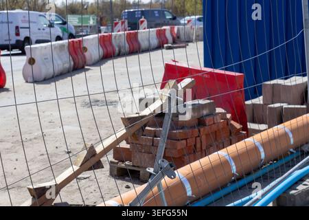 An outdoor view of a fenced construction site with orange plastic barriers, stacked bricks, and plastic pipes, illustrating industrial activity, urban Stock Photo