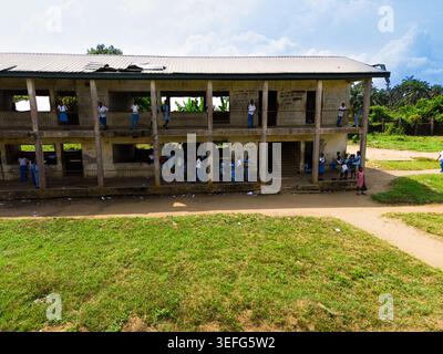 Aerial view of a two-story school building with students in blue uniforms standing on balconies overlooking a grassy field in Ahoada I, Rivers, Nigeri Stock Photo