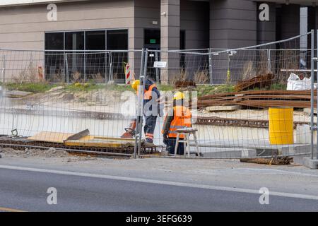 Warsaw, Poland - April 13, 2026: Grupa ZUE crew members cutting concrete on active work site behind metal fencing, emphasizing industrial construction Stock Photo