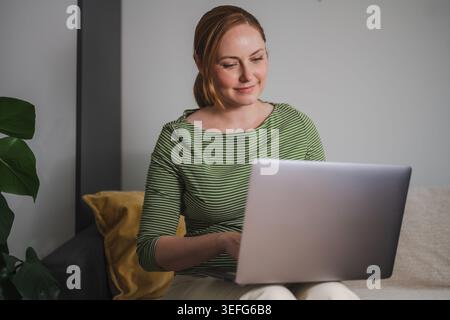 Comfortable remote work concept, woman using laptop from home Stock Photo