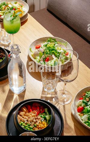Healthy salad bowls and drinks on a sunlit wooden table Stock Photo