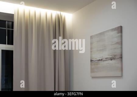Modern room wall adorned with an abstract beige painting beside elegant floor to ceiling drapery, creating a calm atmosphere for sophisticated home de Stock Photo