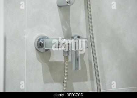 Close up of a sleek metal water mixer valve and flexible hose installed on a neutral grey tile background symbolizing cleanliness and comfort in luxur Stock Photo