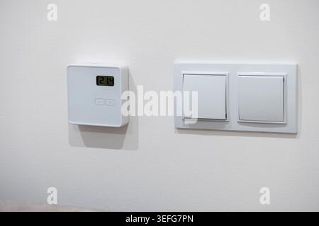 Smart temperature controller next to wall light switches, displaying current indoor heat levels to promote sustainability, energy management, and smar Stock Photo