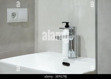 Minimalist bathroom interior with a shiny metal tap and hygiene bottle on a sink, emphasizing cleanliness, residential plumbing, modern home renovatio Stock Photo