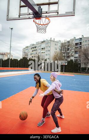 Diverse women friends playing basketball on outdoor court Stock Photo