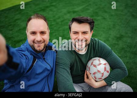 Happy friends taking selfie on soccer field with ball Stock Photo